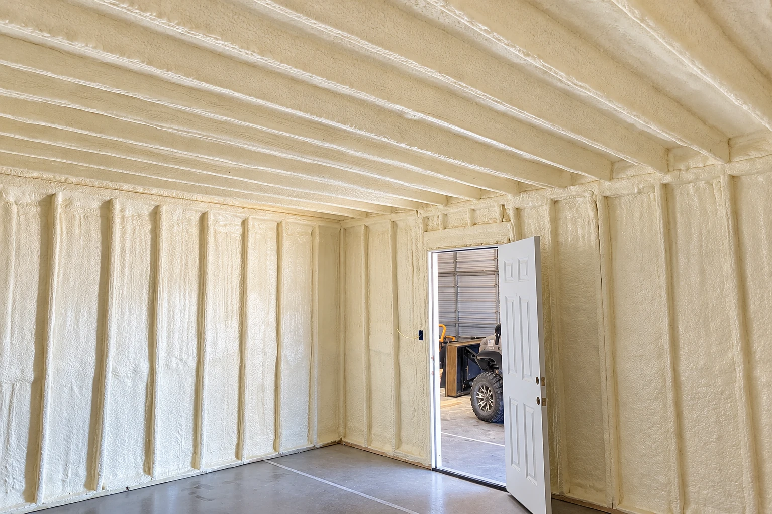 White spray foam covers the walls and ceiling of an unfinished room with an open doorway.