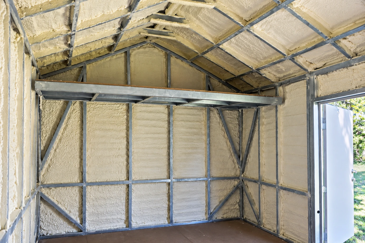 Unfinished room with metal framing and cream-colored spray foam covering the walls and sloped ceiling beside an open doorway.